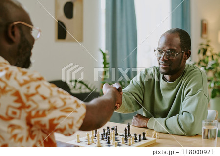 Over shoulder shot of two young African American men doing handshake while playing chess game in living room Over shoulder shot of two young African American men doing handshake while playing chess game in living room 118000921