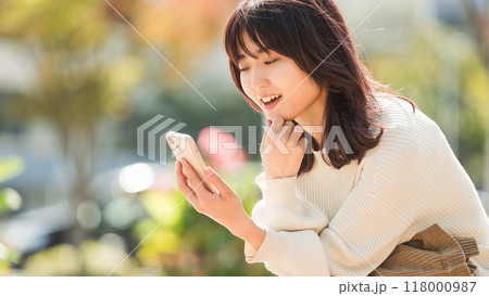 秋の屋外でスマホを見る笑顔の女性 118000987