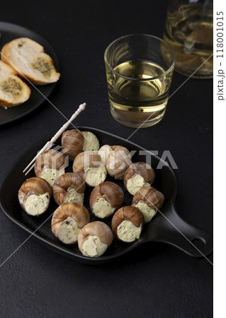 Escargot bourguignon with butter and garlic. Traditional French dish made from snails, served with baguette and white wine. Selective focus, close-up, black background. Escargot bourguignon with butter and garlic. Traditional French dish made from snails, served with baguette and white wine. Selective focus, close-up, black background. 118001015