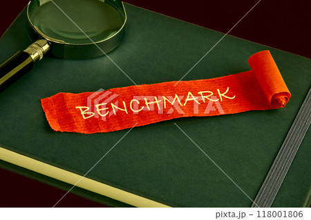 Business concept of benchmark. A word BENCHMARK written on a piece of red paper on the background of a green business book, notebook Business concept of benchmark. A word BENCHMARK written on a piece of red paper on the background of a green business book, notebook 118001806
