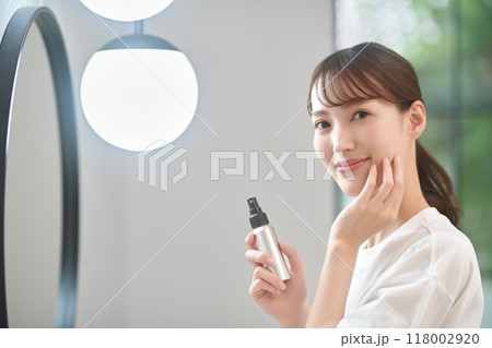洗面所で鏡を見ながらスキンケアをする若い女性 洗面所で鏡を見ながらスキンケアをする若い女性 118002920