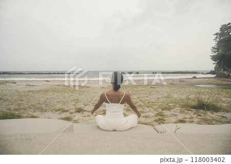 海辺に座ってヨガをしている若い女性 118003402