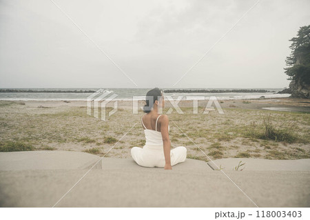 海辺に座ってヨガをしている若い女性 118003403
