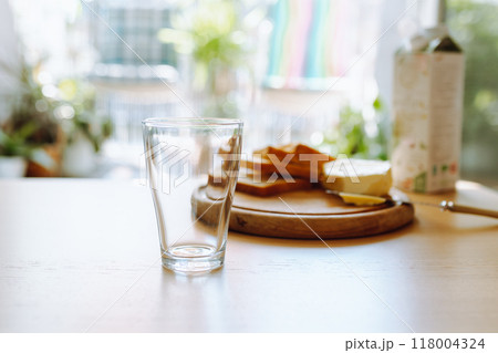 An empty glass stands on table, in background there is bread, butter, milk. Breakfast An empty glass stands on table, in background there is bread, butter, milk. Breakfast 118004324