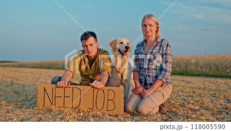 A farmer couple with their Golden Retriever sits in a field, holding a cardboard sign that says Need Job. A farmer couple with their Golden Retriever sits in a field, holding a cardboard sign that says Need Job. 118005590
