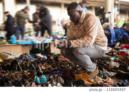 Man in an African sheepskin coat looks at used shoes at a flea market 118005897