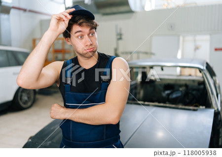 Puzzled mechanic male wondering looking away in auto workshop standing by car under repair. Doubtful repairman trying to solve problem in car service shop. Concept of automobile maintenance. 118005938