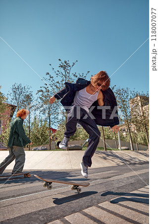 Dynamic image of stylish young boys in motion in public park, on sunny day, skateboarding with energy Blending street style and fashion 118007077