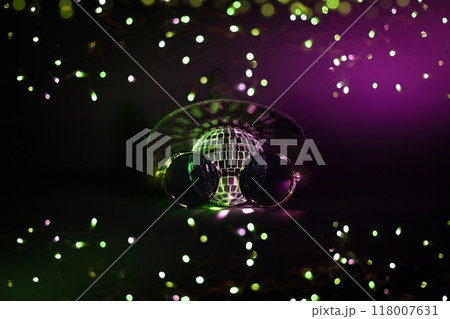 A witch hat and a disco ball and hipster sunglasses with green and purple bokeh light on a black background. Creative Halloween party wallpaper A witch hat and a disco ball and hipster sunglasses with green and purple bokeh light on a black background. Creative Halloween party wallpaper 118007631