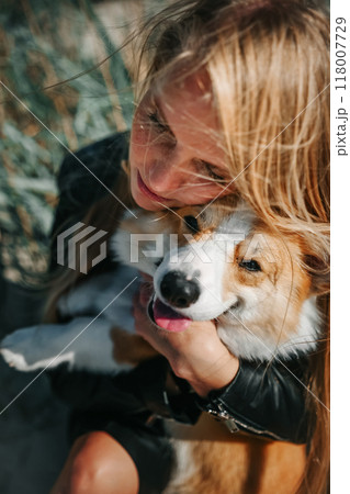A woman enjoys a sunny day at the beach while hugging her corgi in the tall grass A woman enjoys a sunny day at the beach while hugging her corgi in the tall grass 118007729