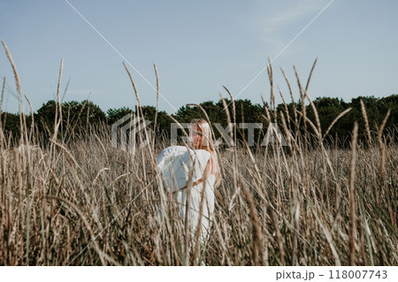 Young blonde woman walks through a field of tall grass wrapped in white blanket 118007743