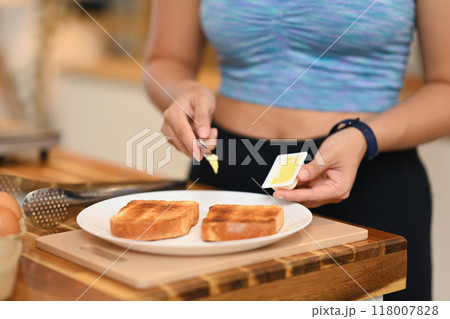 Close up image of young woman spreading butter on a piece of toast Close up image of young woman spreading butter on a piece of toast 118007828
