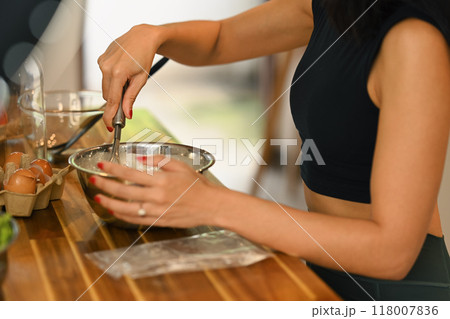 Cropped shot of woman preparing food on a wooden table, mixing ingredients in a metal bowl 118007836