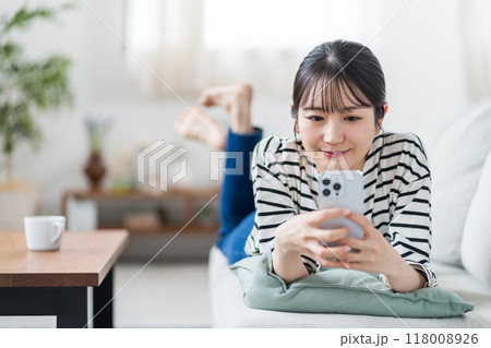 ソファーの上でスマホを操作する若い女性。 118008926