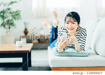 ソファーの上でスマホを操作する若い女性。 ソファーの上でスマホを操作する若い女性。 118008927