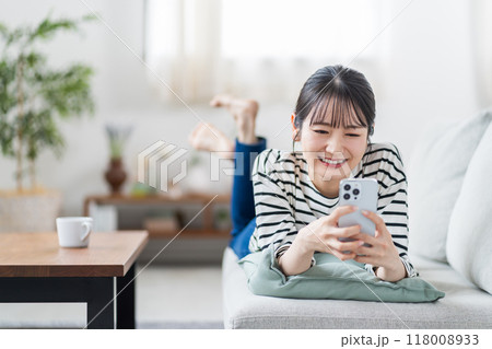 ソファーの上でスマホを操作する若い女性。 ソファーの上でスマホを操作する若い女性。 118008933