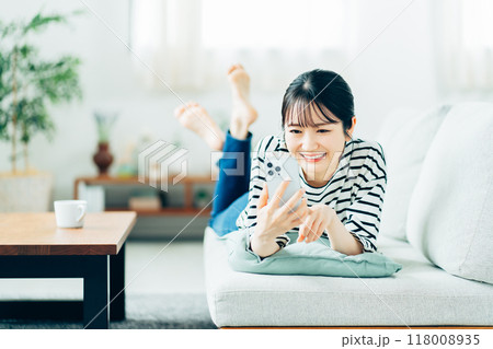ソファーの上でスマホを操作する若い女性。 118008935