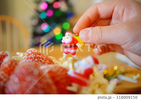 小学生の子供がクリスマスケーキのデコレーションにサンタクロースのピックを飾ろうとしているところ 118009150