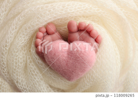 The tiny foot of a newborn baby. Soft feet of a new born in a white wool blanket. Close up of toes, heels and feet of a newborn. Knitted pink heart in the legs of a baby. Studio macro photography. 118009265