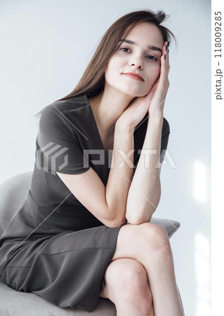 Beautiful fashionable brunette woman in gray summer dress sitting on a chair Beautiful fashionable brunette woman in gray summer dress sitting on a chair 118009285