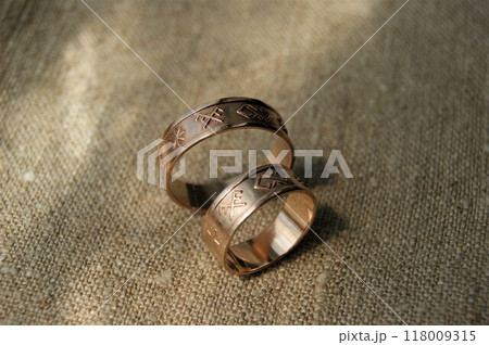 Gold wedding rings with ancient symbols. Rings on linen fabric. Gold wedding rings with ancient symbols. Rings on linen fabric. 118009315