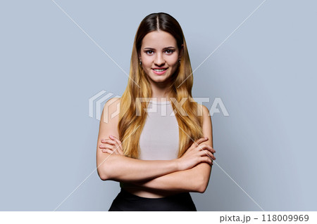 Beautiful young girl with crossed arms looking at camera on gray background Beautiful young girl with crossed arms looking at camera on gray background 118009969