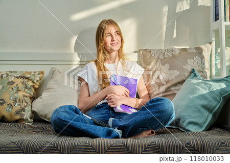 Portrait of female student at home on couch with notebook digital tablet, studying at home 118010033