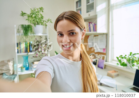 Close-up selfie portrait of teenage cheerful female looking at web camera Close-up selfie portrait of teenage cheerful female looking at web camera 118010037