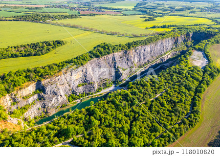 A tranquil morning unfolds over Velka Amerika Quarry, showcasing the impressive rocky cliffs surrounded by lush greenery 118010820