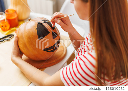 Woman painting face on pumpkin for Halloween Woman painting face on pumpkin for Halloween 118010982