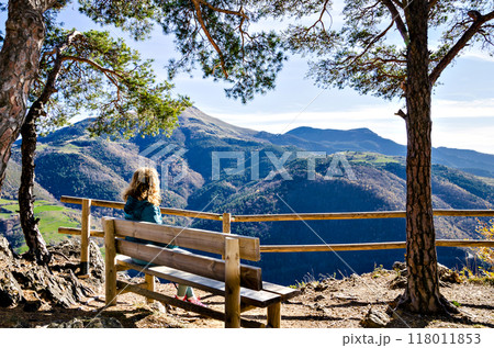 Curly-haired blonde woman, sitting on a bench, looking at the fantastic views of the Ribes mountains, in the Ripolles region, Girona 118011853