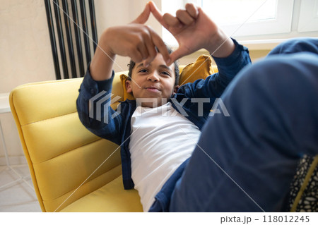 Cheerful boy resting on couch and making capture symbol with hands Cheerful boy resting on couch and making capture symbol with hands 118012245