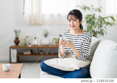 ソファーでスマホを使う若い女性。 118016100