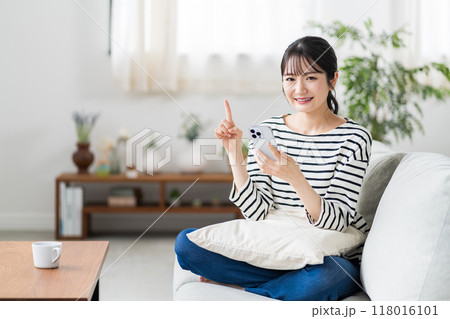 ソファーでスマホを使う若い女性。 118016101