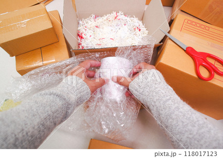 A human hand is wrapping a glass of water in air bubble plastic to prevent A human hand is wrapping a glass of water in air bubble plastic to prevent 118017123