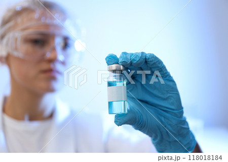 Glass bottle with vaccine in doctor's gloved hand on blue background, close up 118018184