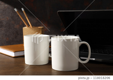 White cups on a wooden table with a laptop White cups on a wooden table with a laptop 118018206