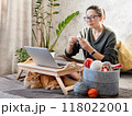 Ginger cat looks how woman is crocheting while watching movie on laptop. Learn to knit from video lessons on Internet. Cozy home and anti stress hobby. 118022001