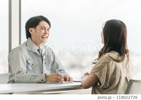 リフォーム・マイホームの相談・打ち合わせに来た女性とカウンセリング・ヒアリングする作業服姿の男性 118022726