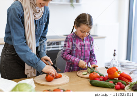 Muslim mother and daughter cutting ingredients for salad in kitchen 118022811