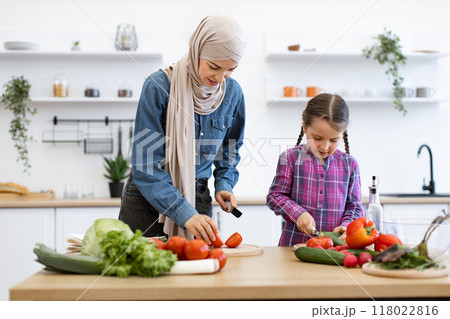 Muslim mother and daughter preparing salad together in kitchen 118022816