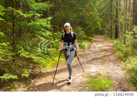 Beautiful woman with Scandinavian sticks hiking in summer through a forest by path. Beautiful woman with Scandinavian sticks hiking in summer through a forest by path. 118024056