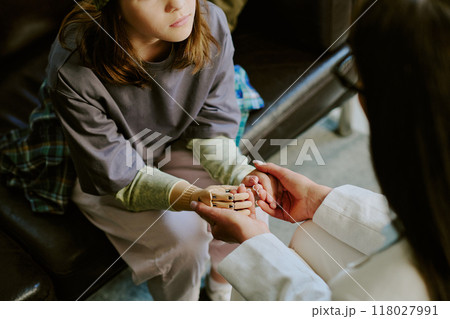 Child sitting on couch, receiving comfort from person holding robotic hand, reflecting support and technological advancement. Details emphasize childs thoughtful expression 118027991