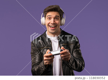 Excited gamer man playing online video game on console with gamepad on violet Excited gamer man playing online video game on console with gamepad on violet 118030352