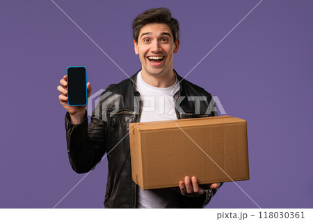 Excited smiling man, online shopping consumer received cardboard order parcel box, desired purchase. Mobile phone, smartphone mockup with copy space screen for your advertisement 118030361