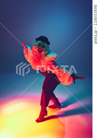 Joyful and eerie, clown dancing, her makeup and costume striking in colored neon lighst against gradient background. 118031698