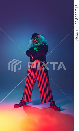 Tall and confident, clown crosses his arms and looking at camera in neon light against gradient background. Tall and confident, clown crosses his arms and looking at camera in neon light against gradient background. 118031718