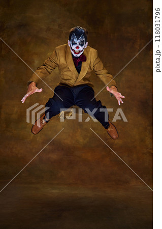 Sinister clown jumps, eyes wide and arms outstretched, as if leaping toward his next victim in neon light against gradient background. Sinister clown jumps, eyes wide and arms outstretched, as if leaping toward his next victim in neon light against gradient background. 118031796