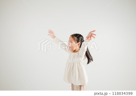 A jubilant kid girl raises her fists in celebration of her success, saying yes with excitement. Asian portrait of a happy young kindergarten child in a studio shot on a white background, winning 118034399