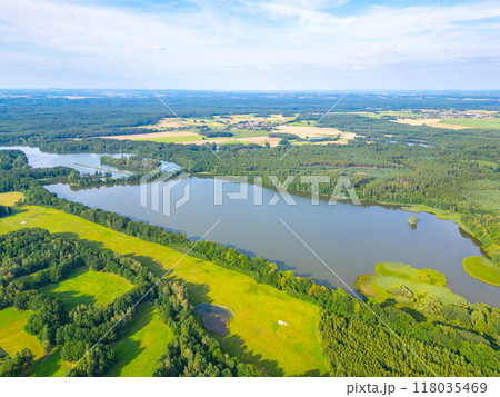 An expansive aerial view showcases the serene rural landscape surrounding Trebon, Czechia, featuring lush green fields, tranquil lakes, and a diverse array of trees under a clear blue sky. 118035469
